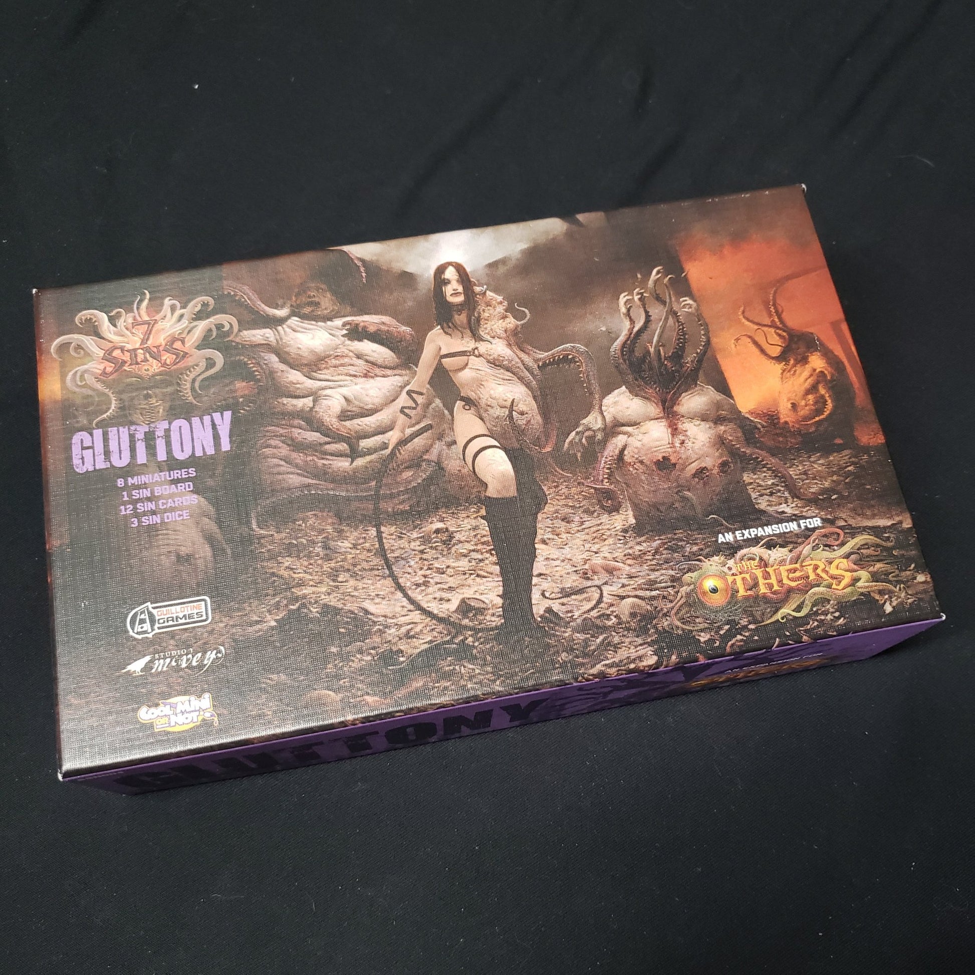 Image shows the front cover of the box of the Gluttony expansion for the board game The Others
