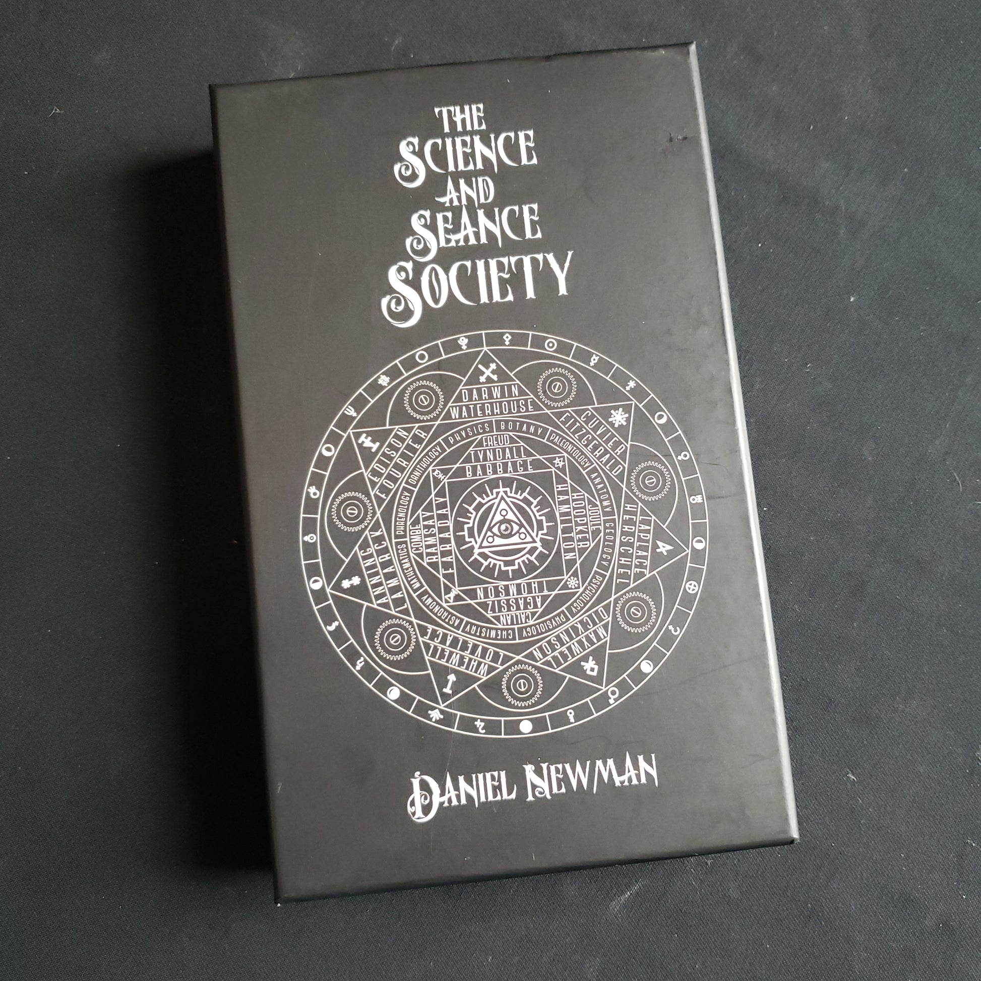 Image shows the front cover of the box of the Science and Seance Society board game