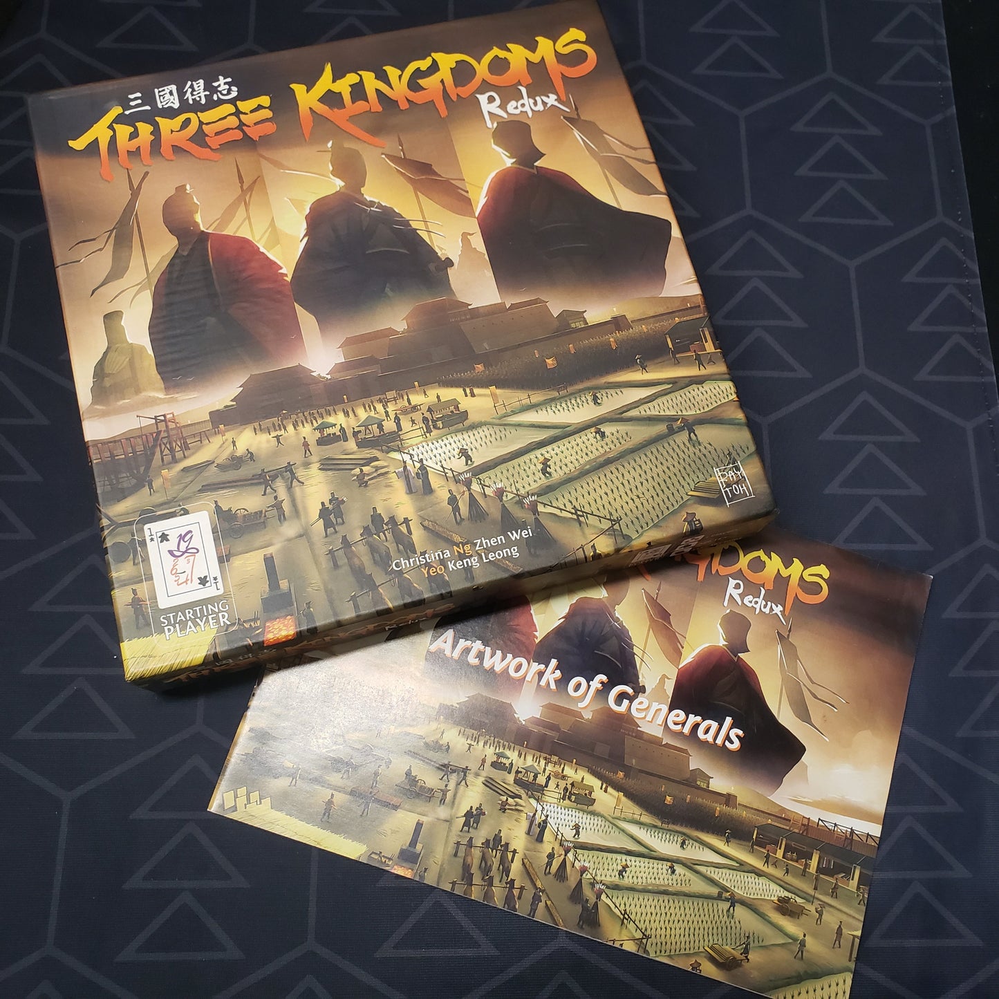 Image shows the front cover of the box for the Three Kingdoms Redux board game sitting on top of the Artwork Of Generals art booklet
