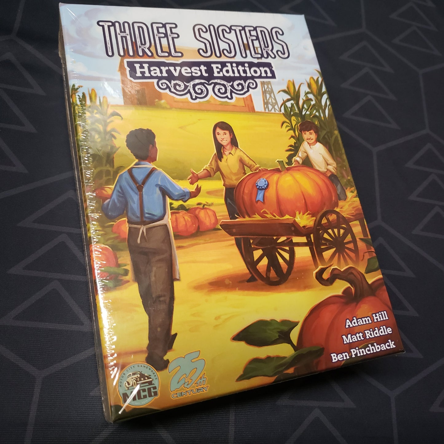 Image shows the front cover of the box for the board game Three Sisters: Harvest Edition