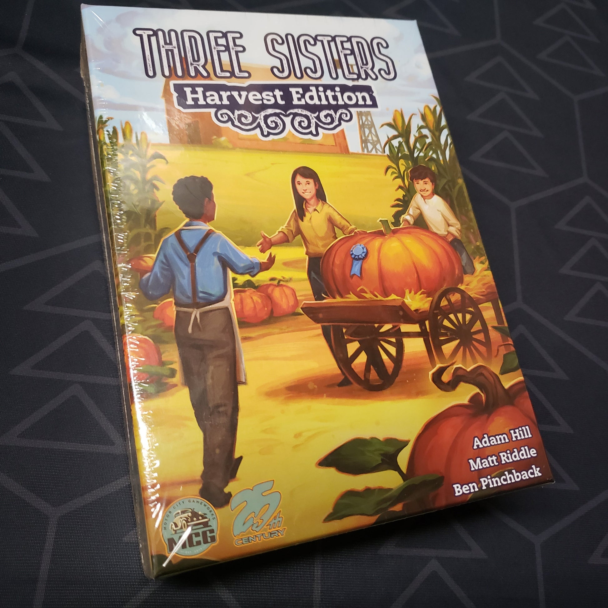 Image shows the front cover of the box for the board game Three Sisters: Harvest Edition
