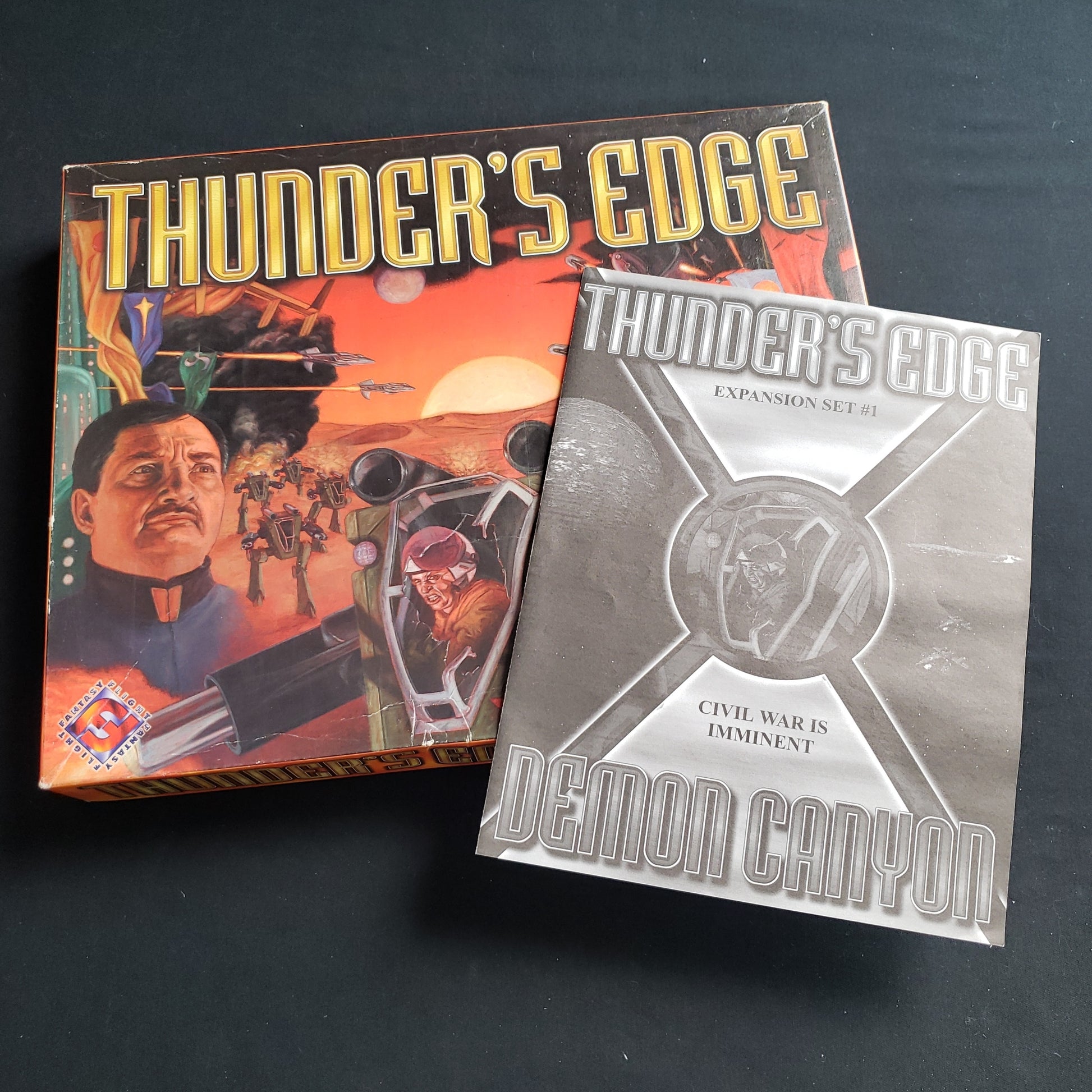 Image shows the front cover of the box of the Thunder's Edge board game, with the instructions for the Demon Canyon expansion sitting on top of it