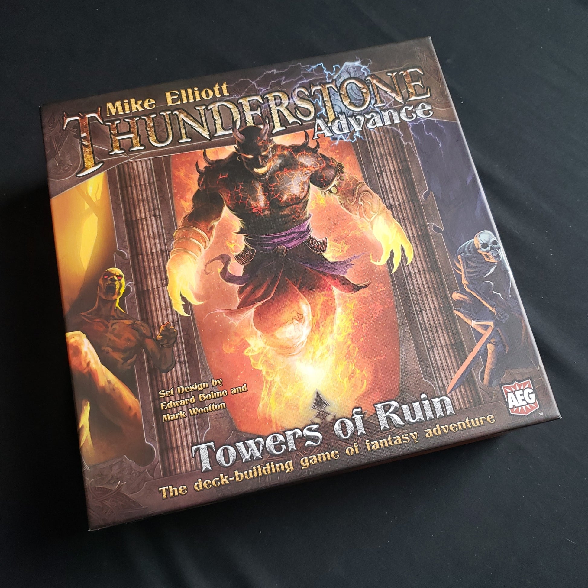 Image shows the front cover of the box of the Thunderstone Advance: Towers of Ruin board game, with the instructions for the Into The Abyss expansion on top of it