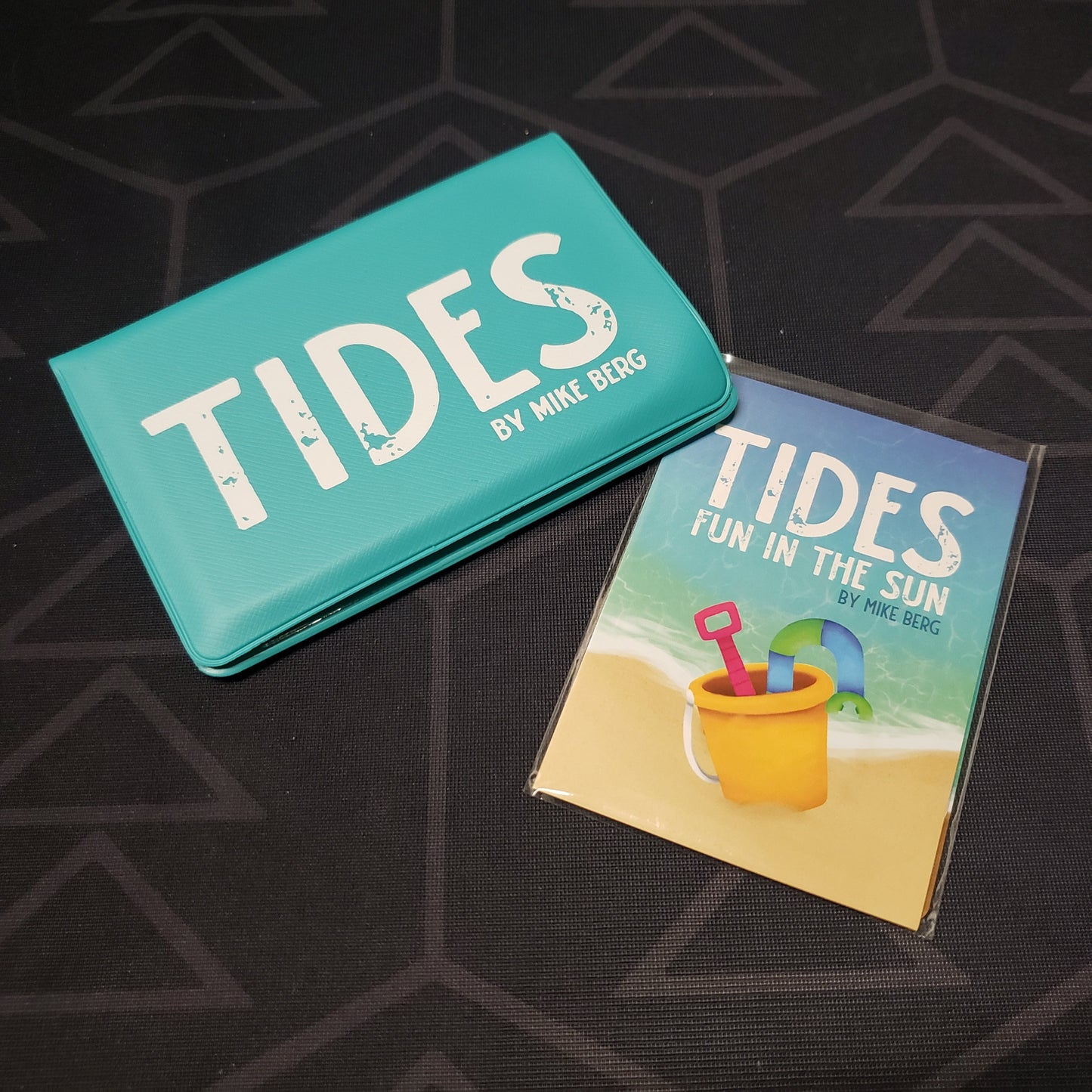 Image shows the front of the card wallet for the Tides card game, with the Fun in the Sun expansion sitting next to it