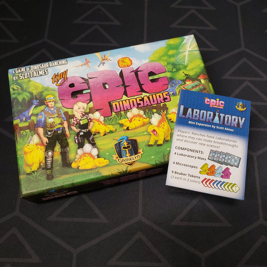 Image shows the front cover of the box of the Tiny Epic Dinosaurs board game with the instructions for the Laboratory mini expansion sitting on top of it