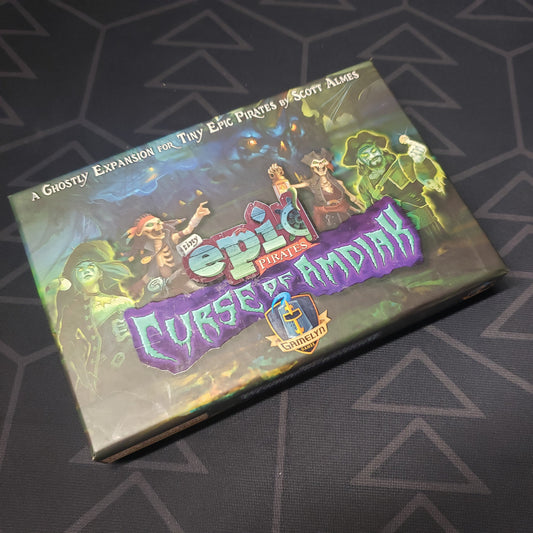 Image shows the front cover of the box of the Curse of Amdiak expansion for the board game Tiny Epic Pirates