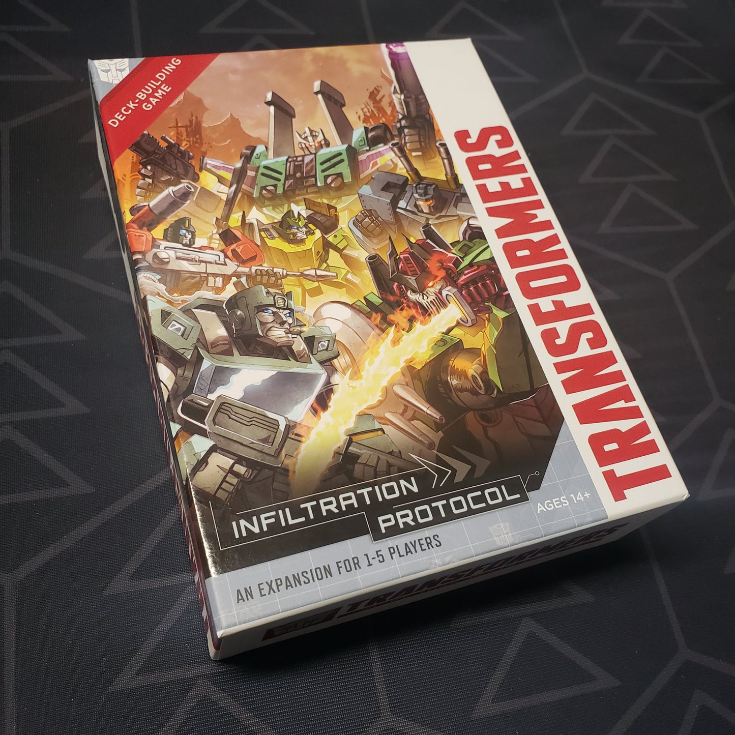 Image shows the front cover of the box of the Infiltration Protocol expansion for the card game Transformers Deck-Building Game