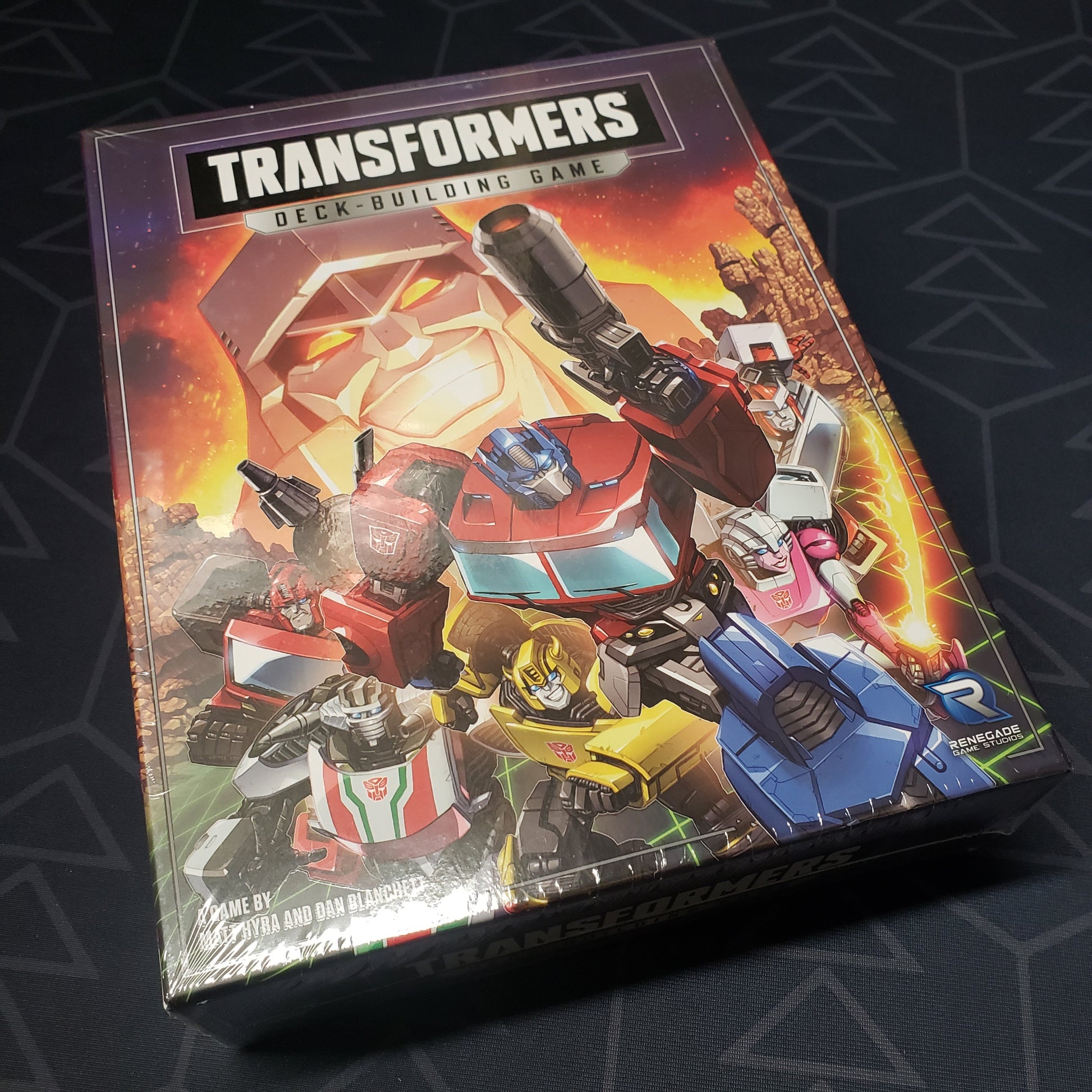 Image shows the front cover of the box of the Transformers Deckbuilding game
