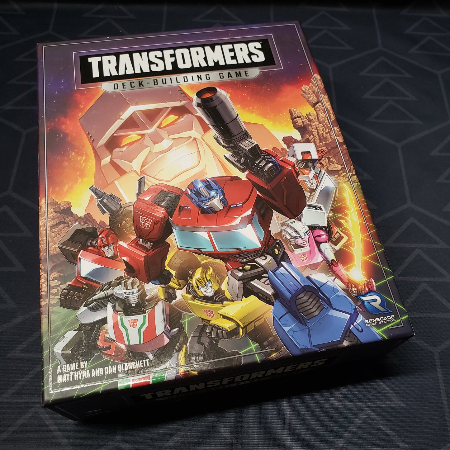 Image shows the front cover of the box of the Transformers Deckbuilding game