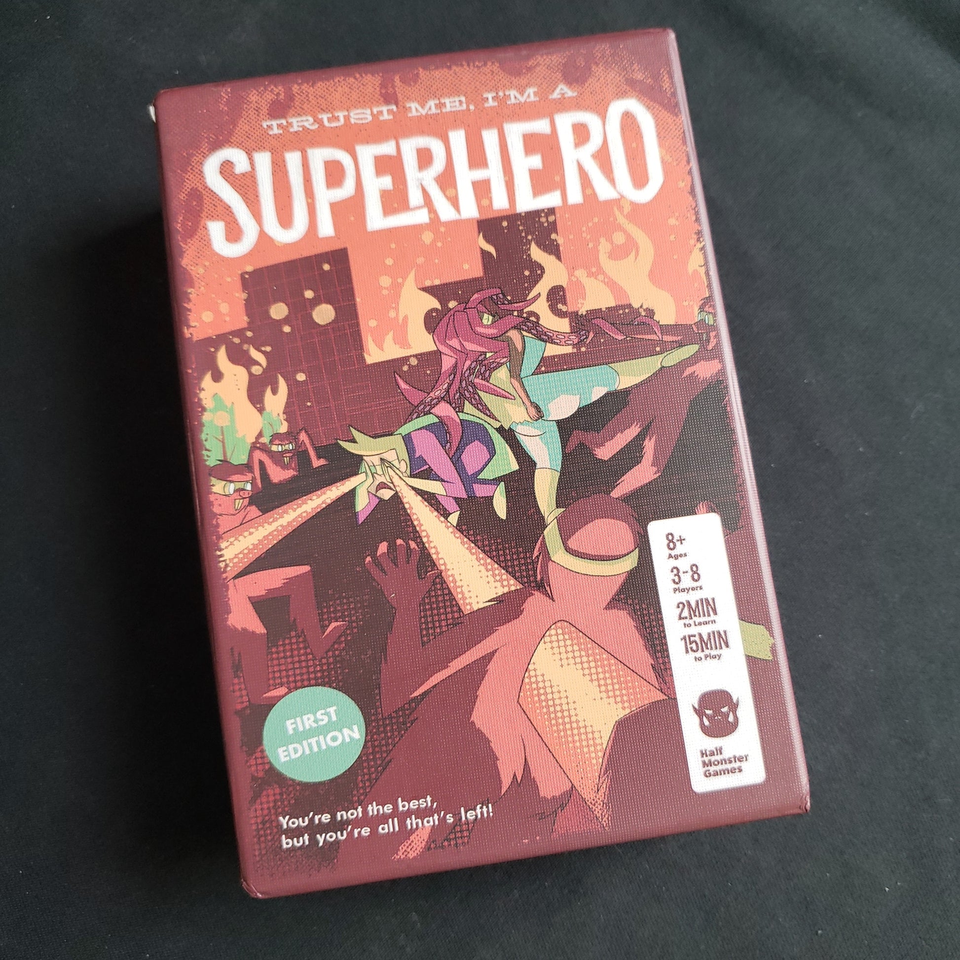 Image shows the front cover of the box of the card game Trust Me, I'm A Superhero