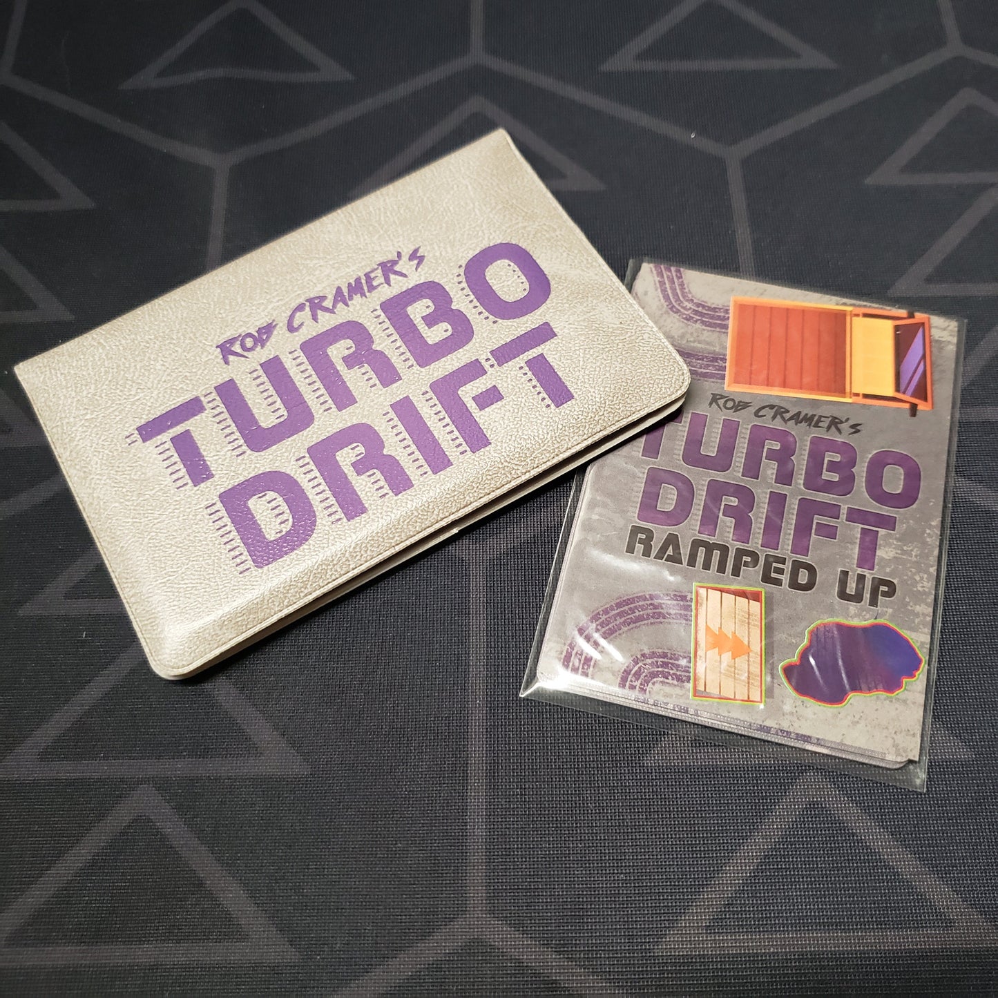 Image shows the front of the card wallet for the Turbo Drift card game, with the Ramped Up expansion sitting next to it
