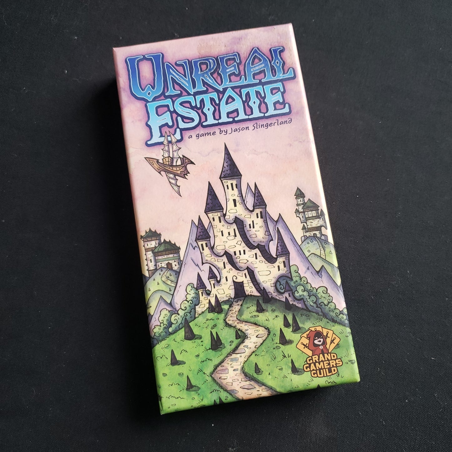 Image shows the front cover of the box of the Unreal Estate card game