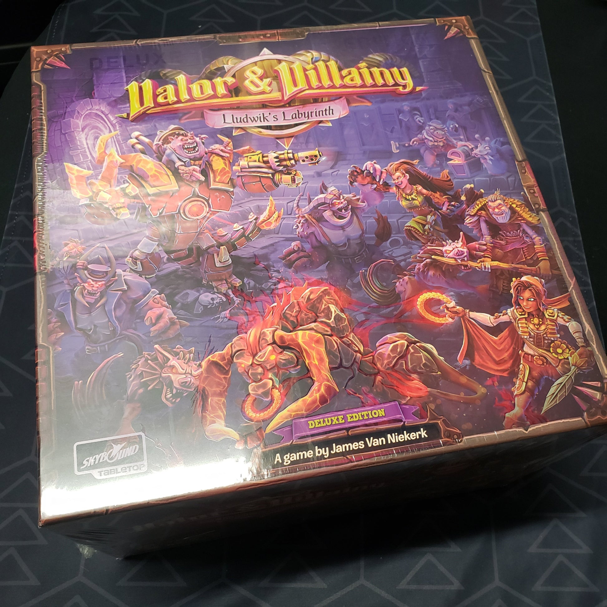 Image shows the front cover of the Deluxe Edition box for the board game Valor & Villainy: Lludwik's Labyrinth
