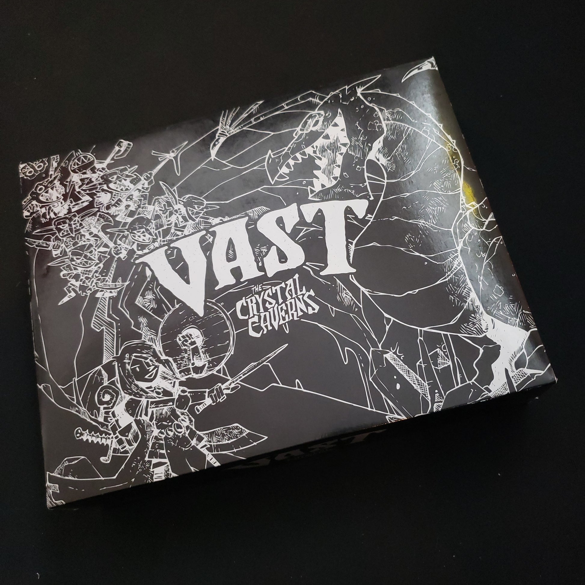 Image shows the alternate black slipcase front cover of the box of the Vast: The Crystal Caverns board game