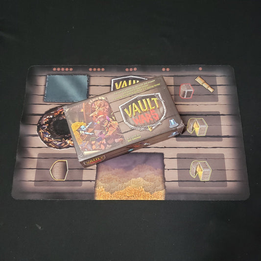 Image shows the front cover of the box of the Vault Wars card game sitting on top of the playmat for the game