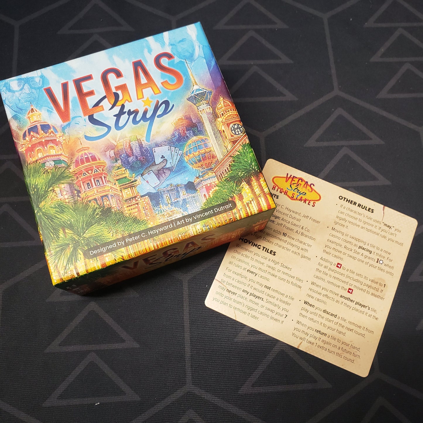 Image shows the front cover of the box for the Vegas Strip board game with the instructions for the High Stakes expansion sitting next to it