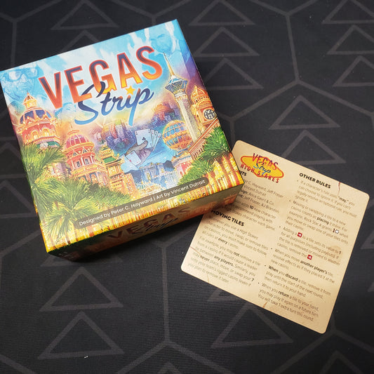 Image shows the front cover of the box for the Vegas Strip board game with the instructions for the High Stakes expansion sitting next to it
