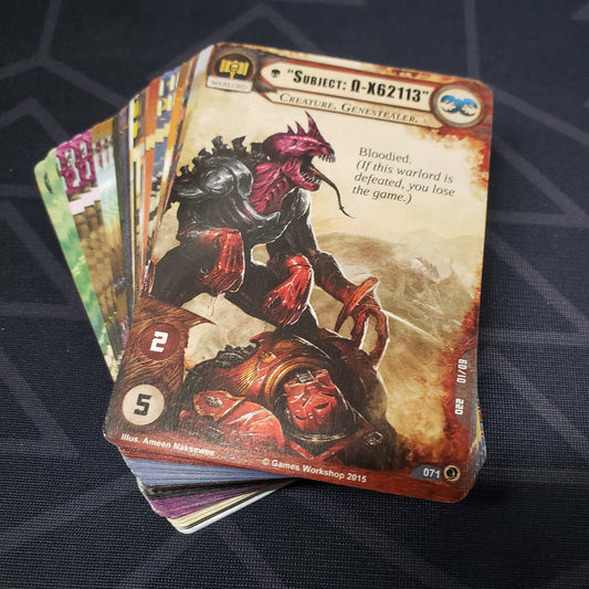 Image shows the cards for the What Lurks Below expansion for the card game Warhammer 40K Conquest fanned out in a stack