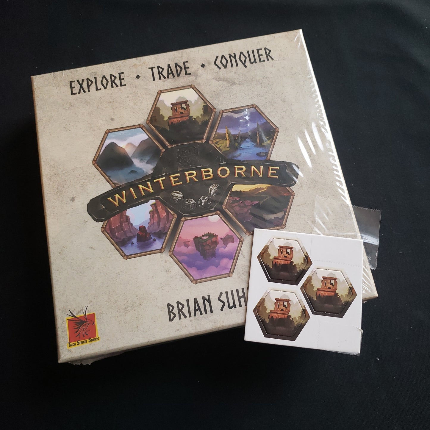 Image shows the front cover of the box of the Winterborne board game, with a card of bonus hex tiles sitting on top of it