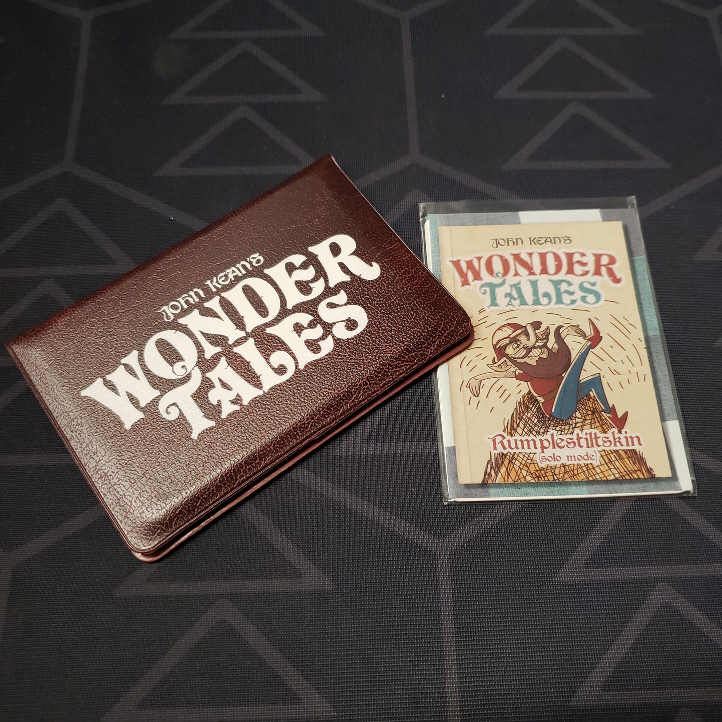 Image shows the front of the card wallet for the Wonder Tales card game, with the Rumpelstiltskin solo expansion sitting next to it