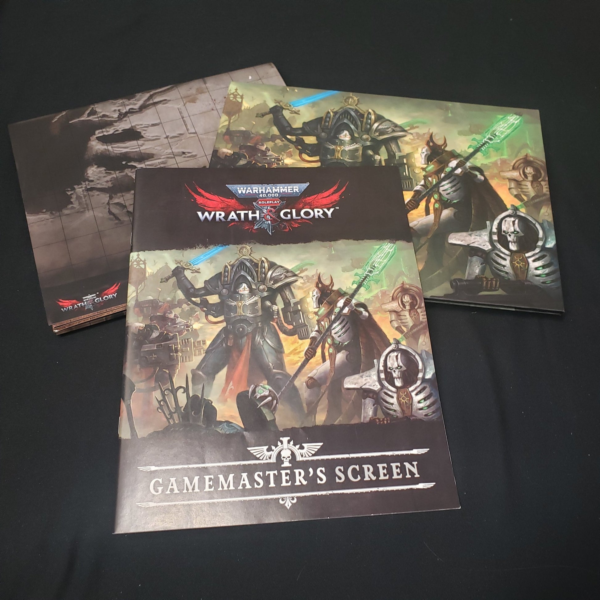 Image shows a scenario book, battlemat, and gamemaster screen for the roleplaying game Wrath & Glory