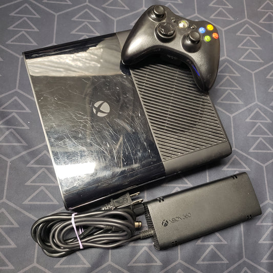 Image shows the top of a Xbox 360 E gaming console with a controller sitting on top and power supply sitting beside it