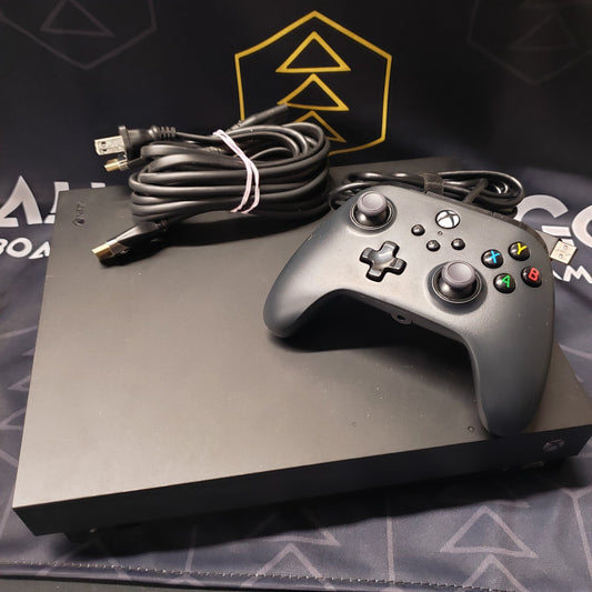 Image shows the top of a Xbox One X gaming console with a wired controller and cables wrapped up on top of it