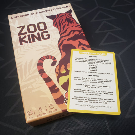 Image shows the front cover of the box for the Zoo King card game with the instruction card for the Zoovenirs expansion sitting on top of it