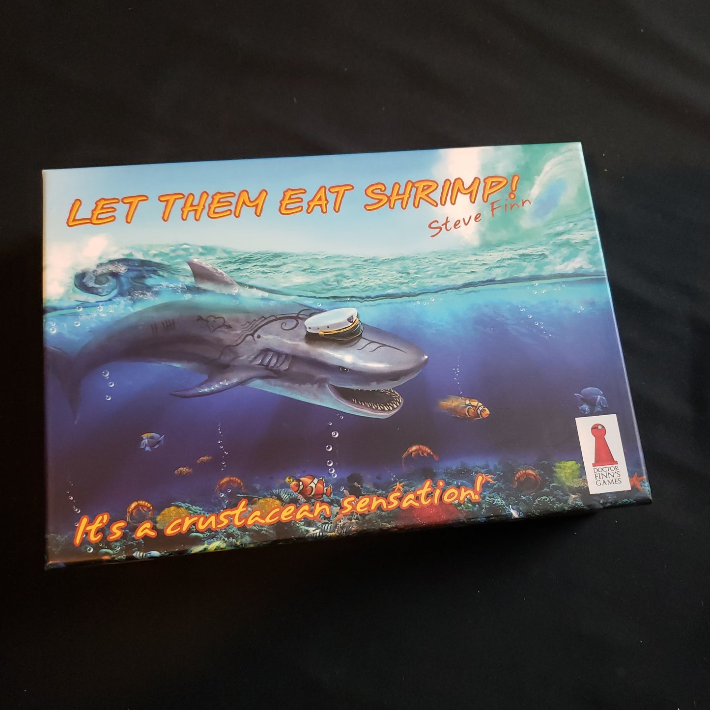 Image shows the front cover of the box of the Let Them Eat Shrimp! board game