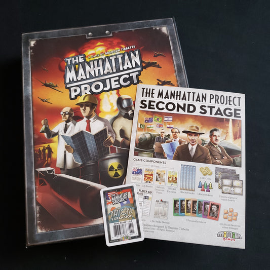 Image shows the front cover of the box of the Manhattan Project board game, along with the instructions for the Second Stage expansion and Nations barcode card