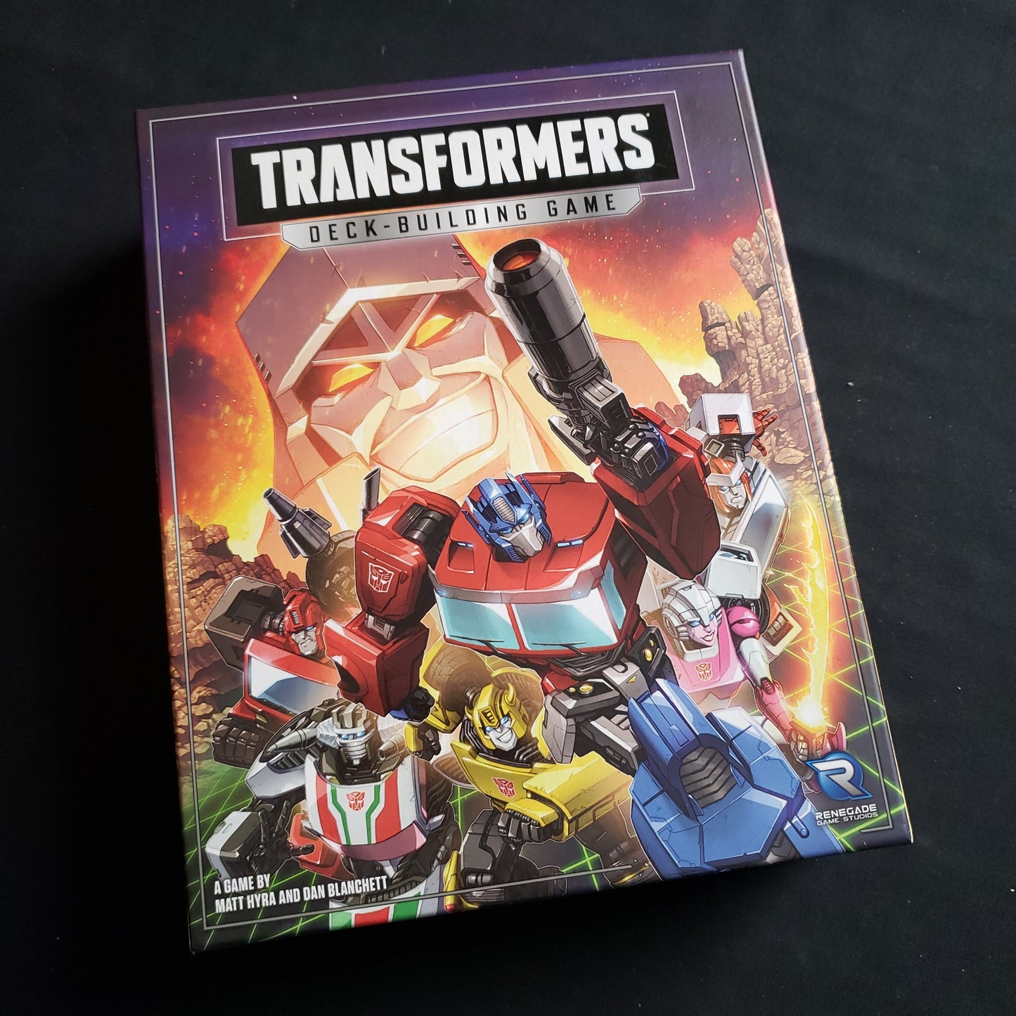 Image shows the front cover of the box of the Transformers Deckbuilding game